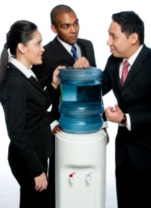 Three colleagues stand around a water cooler gossiping